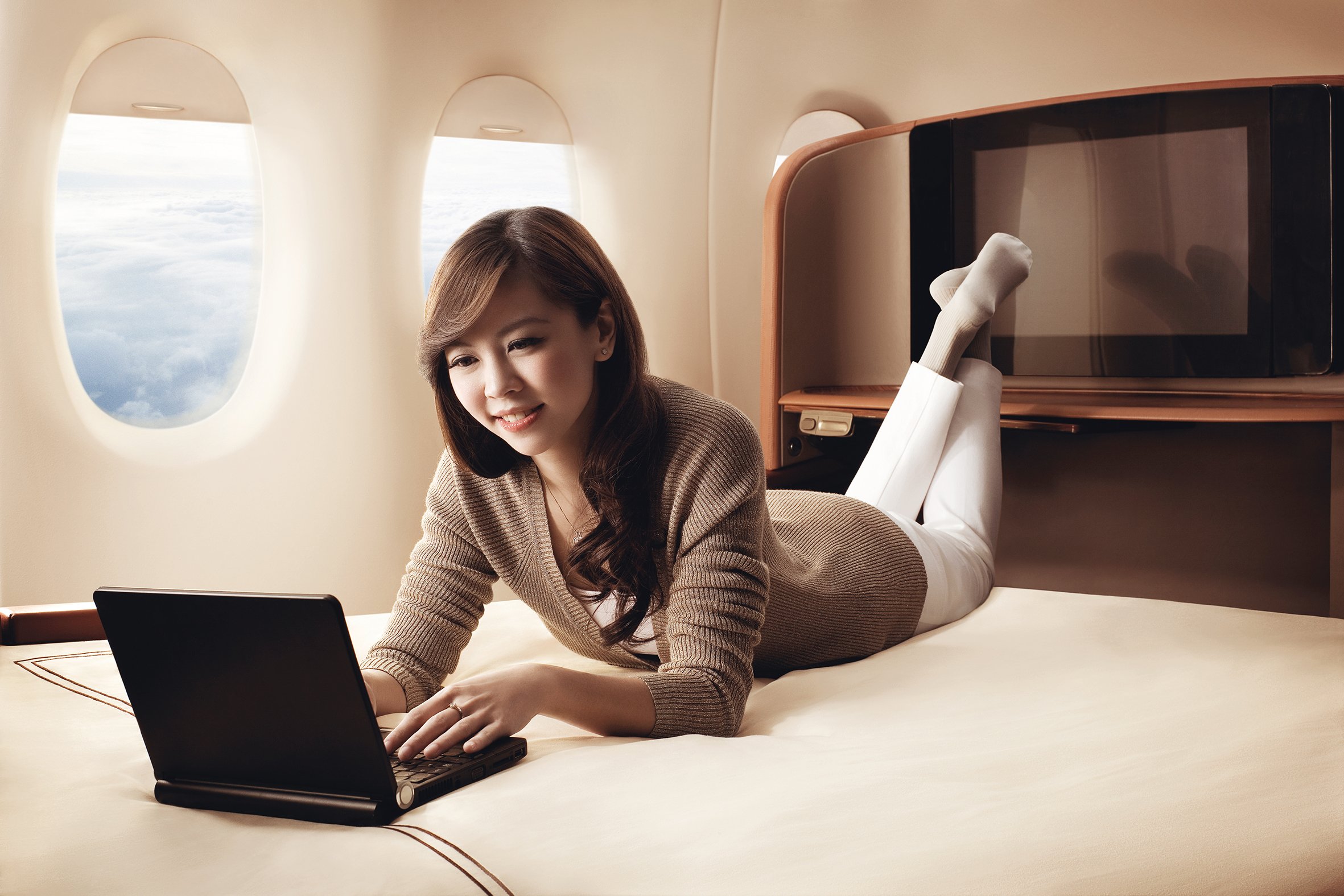 A traveller relaxing with a laptop in a first-class cabin suite, above the clouds